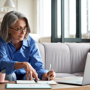 Smiling 60s middle aged business lady using computer watching webinar